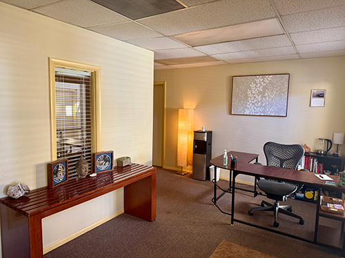 The welcoming reception area at HazMatt Holistic Healing in Flagstaff, Arizona, featuring a check-in desk, warm lighting, calming décor, a Buddha statue, jewelry, plants, natural crystals, and a peaceful environment for clients before their massage session.