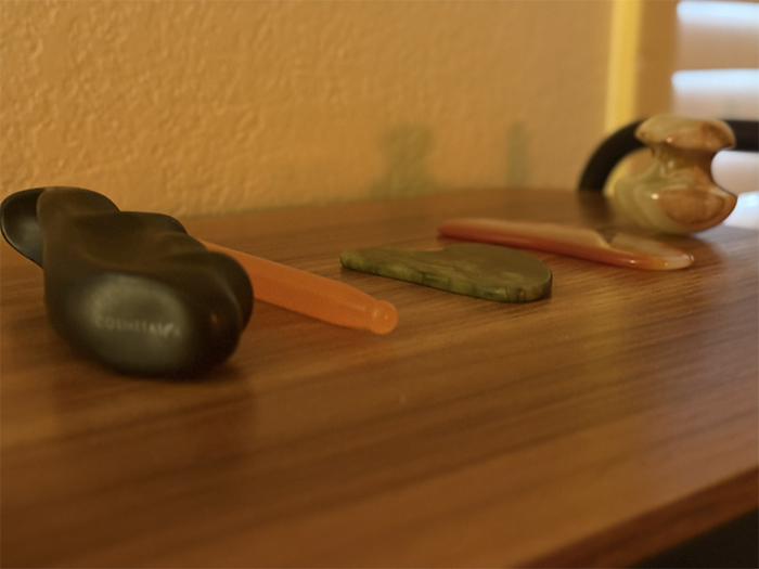 A close-up of massage therapy tools used at HazMatt Holistic Healing in Flagstaff, Arizona, arranged on a wooden shelf, including gua sha tools, a reflexology wand, thumb savers, and basalt hot stones used to complement therapeutic massage sessions.